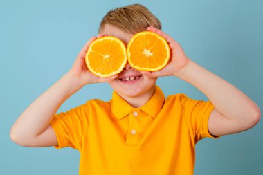 Olumlu duygular. Gözlerinde turuncu olan süpriz bir çocuk. Elleriyle portakalın iki yarısını tutan neşeli bir çocuk. Mavi arka planda izole edilmiş. Sarı tişörtlü çocuk. Yüksek kalite fotoğraf