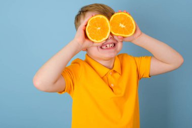 Olumlu duygular. Gözlerinde turuncu olan süpriz bir çocuk. Elleriyle portakalın iki yarısını tutan neşeli bir çocuk. Mavi arka planda izole edilmiş. Sarı tişörtlü çocuk. Yüksek kalite fotoğraf