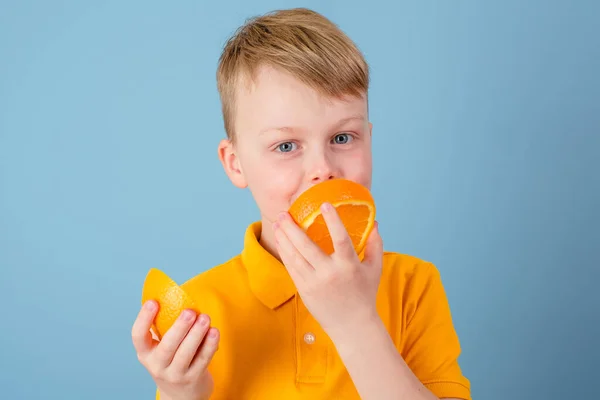 拿着半个橙子的正面男孩 积极的情绪 被蓝色的背景隔离了穿着黄色T恤的小孩高质量的照片 — 图库照片