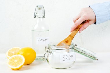 Female hand taking baking soda in jar wooden spoon on a white table. The concept organic stain removers. High quality photo