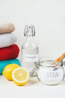 Baking soda in jar with a wooden spoon on top, vinegar, cut lemon, folded towel on a white background. The concept of organic removing stains on clothes. High quality photo