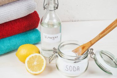 Baking soda in jar with a wooden spoon on top, vinegar, cut lemon, folded towel on a white background. The concept of organic removing stains on clothes. High quality photo