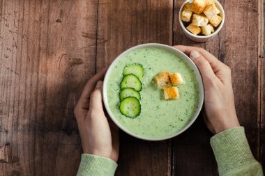 Bir tabak salatalıklı gazpacho tutan kadın elleri. Tahta bir masada, üst manzaralı. Sağlıklı vejetaryen yemeği. - Evet. Yüksek kalite fotoğraf