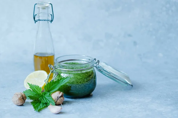 Vegan nettle pesto with garlic, lemon, olive oil and walnut. Open jar of homemade nettle pesto on a gray background. — Stock Photo, Image