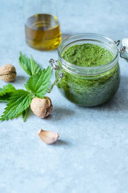 Vejetaryen ısırgan otu, sarımsak, zeytinyağı ve ceviz. Gri arka planda ev yapımı ısırgan otu pesto kavanozu. Vejetaryen ısırgan otu pesto