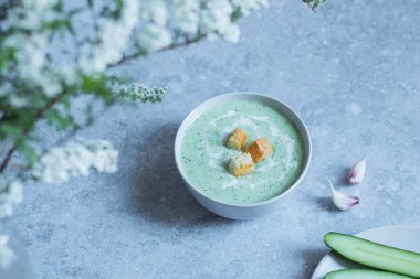 Salatalık çorbası kasede, gri masa arkasında.