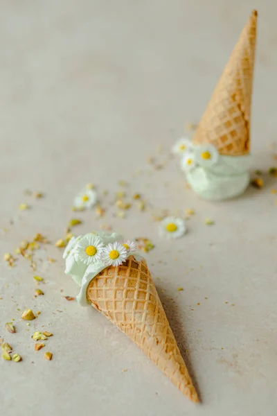 Pistachio ice cream in a horn is decorated with chamomile flowers and scattered nuts. Summer seasonal cold sweet healthy dessert. flat lay . High quality photo