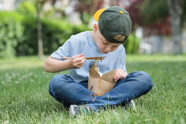 孩子们坐在草地上吃街头食物 他T恤上的酱汁污渍面条落在他的衣服上 高质量的照片 — 图库照片