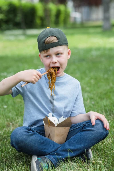 The child eating on the go soy sauce pan-fried noodles chopsticks. Dirty soy sauce stains on a white t-shirt. Takeaway food. outdoors. High quality photo