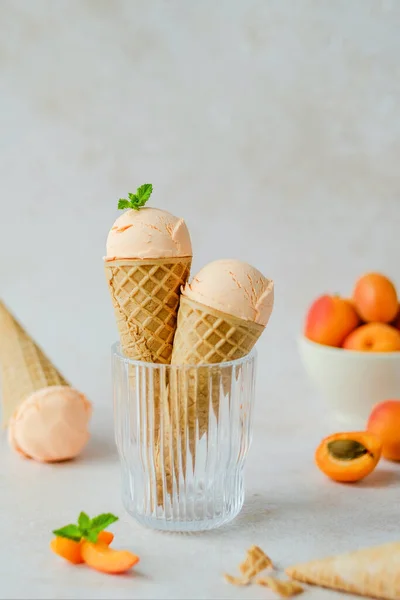 Creamy vegan apricot ice cream in the horn in a glass, styling mint leaves on top. Waffle cone horn upside down. Summer seasonal cold sweet healthy vegan dessert. High quality photo