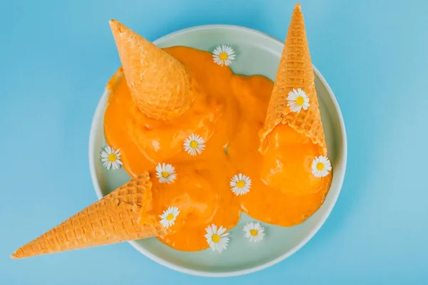 Homemade vegan apricot ice cream in the corner melted on the plate, decorated with daisies on a blue background. Healthy vegan frozen dessert