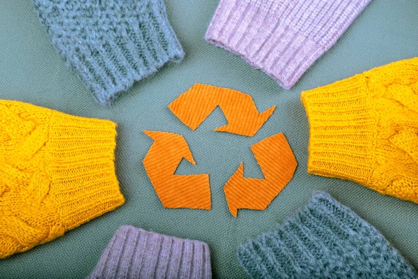 Recycling of clothes. Used clothes. Sleeves of knitted sweaters on a green background. Sustainable fashion and manufacturing