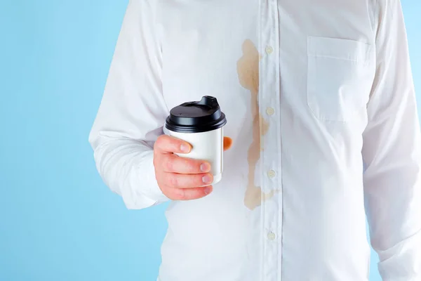 Eco cup of coffee in a man\'s hand on a blue background. Dirty coffee stain on a white clothes. Spoiled clothes. . High quality photo