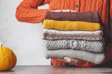 A woman holding a stack autumn warm knitted sweaters. Change of season and wardrobe. autumn slow fashion concept. High quality photo clipart