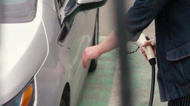 Erkek el, elektrikli araca şarj kablosu takıyor ve pilleri şarj ediyor. Otoparktaki EV istasyonu. Tanınmayan adam güç bağlantısını EV arabasına yerleştiriyor.