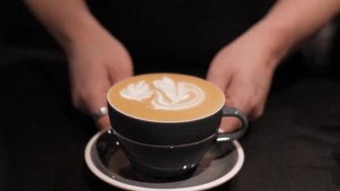 Siyah arka planda sanat kahveli latte, yakın plan. Erkek eller kapuçinoyu köpük boyayla hareket ettirir, boşluğu kopyala