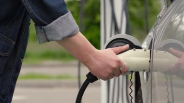 Tanınmayan adam güç bağlantısını EV vagonuna bağlıyor. Erkek el, şarj kablosunu elektrikli araca bağlar, şarj pillerini bitirir. Otoparktaki EV istasyonu