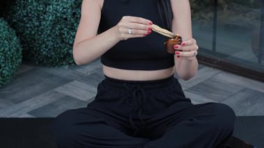 Tanınmayan bir kadın ahşap bir palo santo çubuğu yakıyor, etrafa duman ve koku yayıyor. Yoga yapan siyah elbiseli kadın enerji alanlarını temizliyor.