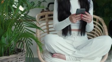 Tanımlanamayan beyaz elbiseli bir kadın, yeşil elbiseli bir sandalyede bağdaş kurup oturuyor ve elinde telefon, evde dinleniyor, akıllı telefondan arkadaşlarıyla sohbet ediyor.