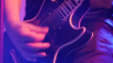 Elektro gitar çalan ellerin yakın çekimi. Çerçevenin sonundaki çok renkli kulüp ışıklarıyla bir defokus ile gitar çalmak