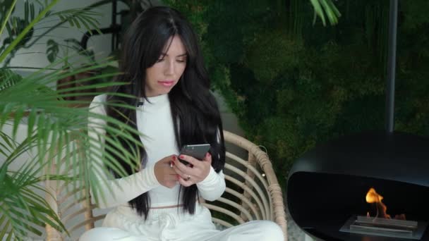 Beautiful Woman White Clothes Holding Phone Sits Chair Room Greenery — Stok video