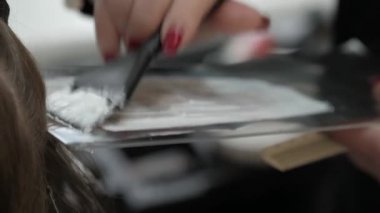 Strand of female hair on a special sheet of foil, the master applies hair dye with a brush. Process of highlighting by a professional master in a beauty salon. Paint hair close-up