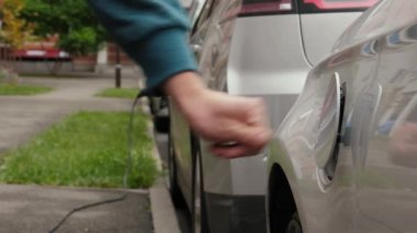 Erkek el, elektrikli bir otoparkta EV 'ye güç bağlantısı kuruyor. Tanınmayan adam şarj aletinin kapağını açar ve kabloyu elektrikli arabaya bağlar ve pilleri şarj eder.