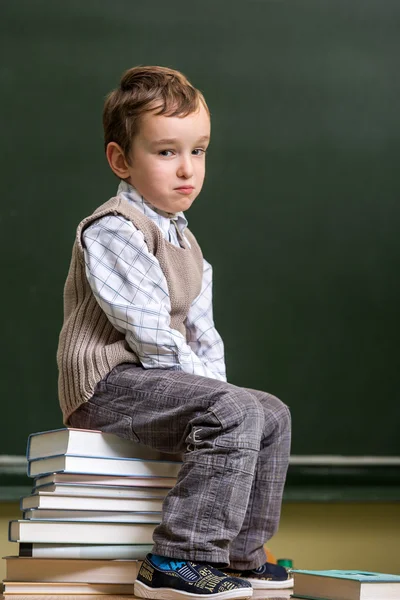 Colegial sentado en un montón de libros en el aula — Foto de Stock