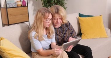Beyaz saçlı büyükanne ve torununun portre resmi rahat bir odada kanepede oturup tablet bilgisayarın ekranından bir şey izlerken.