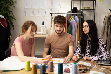 Moda tasarımcılarının ve terzilerin işi. Moda tasarımcıları stüdyolarında çalışıyor. Renkli Kumaşlar, Giysiler Asılma ve Dikiş Ögeleri Görünür.