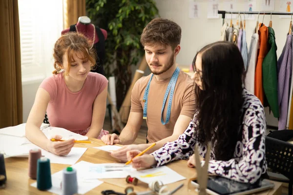 Le travail du créateur de mode et des tailleurs dans la boutique. Créateurs de mode travaillant dans leur atelier. Les tissus colorés, les vêtements suspendus et les articles à coudre sont visibles. Photos De Stock Libres De Droits