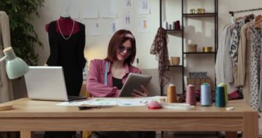 Moda tasarımcılarının ve terzilerin işi. Moda tasarımcıları stüdyolarında çalışıyor. Renkli Kumaşlar, Giysiler Asılma ve Dikiş Ögeleri Görünür
