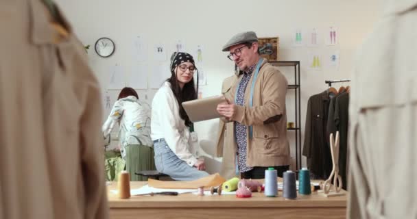 El trabajo del diseñador de moda y sastres en la tienda. Diseñadores de moda trabajando en su estudio. Tejidos coloridos, ropa colgante y artículos de costura son visibles — Vídeos de Stock