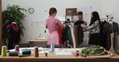 Moda tasarımcılarının ve terzilerin işi. Moda tasarımcıları stüdyolarında çalışıyor. Renkli Kumaşlar, Giysiler Asılma ve Dikiş Ögeleri Görünür