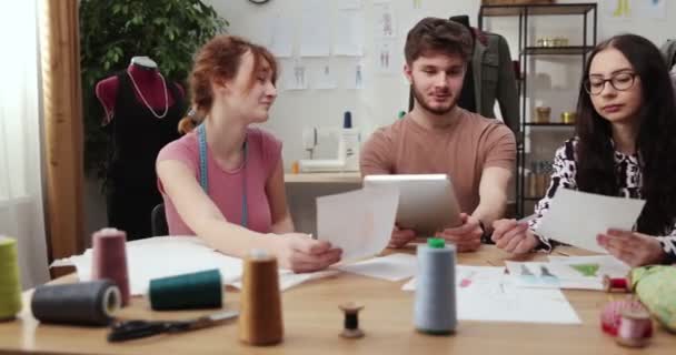 El trabajo del diseñador de moda y sastres en la tienda. Diseñadores de moda trabajando en su estudio. Tejidos coloridos, ropa colgante y artículos de costura son visibles — Vídeos de Stock