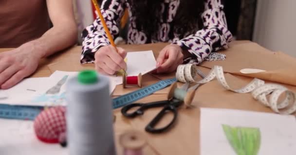 El trabajo del diseñador de moda y sastres en la tienda. Diseñadores de moda trabajando en su estudio. Tejidos coloridos, ropa colgante y artículos de costura son visibles — Vídeos de Stock