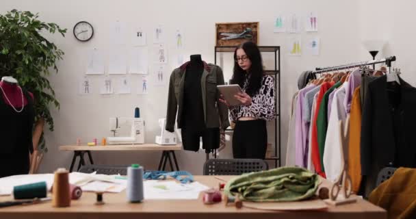 Die Arbeit von Modedesignern und Schneidern im Geschäft. Modedesigner arbeiten in ihrem Atelier. Bunte Stoffe, Kleiderbügel und Nähartikel sind sichtbar. — Stockvideo