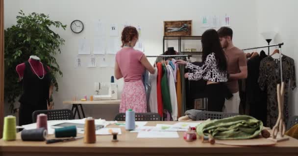 O trabalho do designer de moda e alfaiates na loja. Designers de moda trabalhando em seu estúdio. Tecidos coloridos, roupas penduradas e itens de costura são visíveis. — Vídeo de Stock