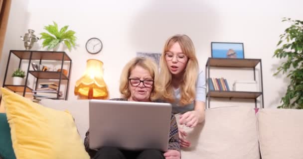 Widok z boku na starą białą babcię i wnuczkę korzystających z laptopa w wygodnym domu. Kobieta wnuczka uczy starszą babcię korzystać z laptopa 4k — Wideo stockowe