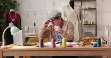 Moda tasarımcılarının ve terzilerin işi. Moda tasarımcıları stüdyolarında çalışıyor. Renkli Kumaşlar, Giysiler Asılma ve Dikiş Ögeleri Görünür.