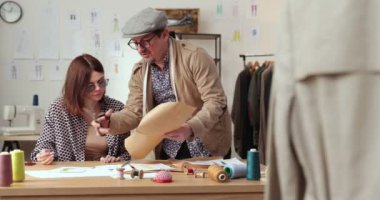 Moda tasarımcılarının ve terzilerin işi. Moda tasarımcıları stüdyolarında çalışıyor. Renkli Kumaşlar, Giysiler Asılma ve Dikiş Ögeleri Görünür.
