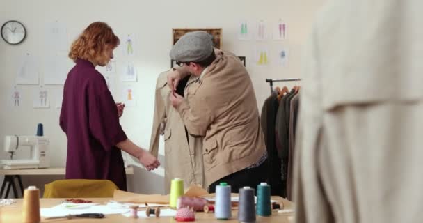 O trabalho do designer de moda e alfaiates na loja. Designers de moda trabalhando em seu estúdio. Tecidos coloridos, roupas penduradas e itens de costura são visíveis. — Vídeo de Stock