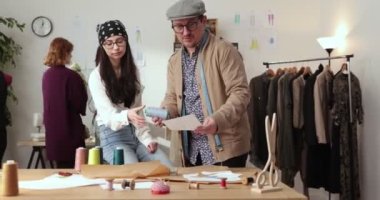 Moda tasarımcılarının ve terzilerin işi. Moda tasarımcıları stüdyolarında çalışıyor. Renkli Kumaşlar, Giysiler Asılma ve Dikiş Ögeleri Görünür.