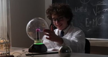 Fizik laboratuvarı: beyaz önlüklü ve gözlüklü yakışıklı genç bilim adamı elektrik testleri yapıyor. Laboratuvarda elektriksel deşarj okuyan bir çocuk.