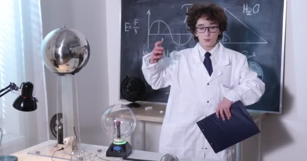 Наукова лабораторія фізики: гарний молодий вчений з білого пальто та окулярів проводить електричні тести. Дитина вивчає електричні розряди в лабораторії . — стокове відео