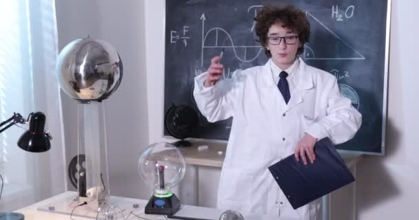 Laboratorio de Ciencias Físicas: guapo joven científico con bata blanca y gafas haciendo pruebas eléctricas. Niño estudiando descargas eléctricas en un laboratorio. — Vídeos de Stock