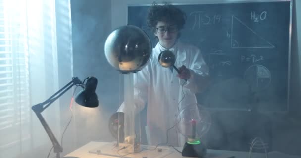 Fysica wetenschapslab: knappe jonge wetenschapper in witte jas en bril doet elektrische tests. Kind bestudeert elektrische ontladingen in een lab. — Stockvideo