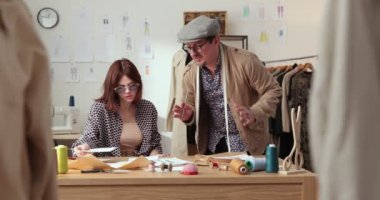 Moda tasarımcılarının ve terzilerin işi. Moda tasarımcıları stüdyolarında çalışıyor. Renkli Kumaşlar, Giysiler Asılma ve Dikiş Ögeleri Görünür.