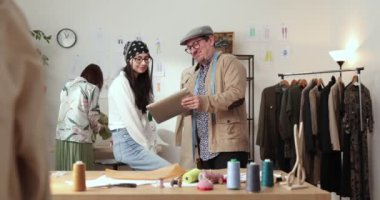 Moda tasarımcılarının ve terzilerin işi. Moda tasarımcıları stüdyolarında çalışıyor. Renkli Kumaşlar, Giysiler Asılma ve Dikiş Ögeleri Görünür.