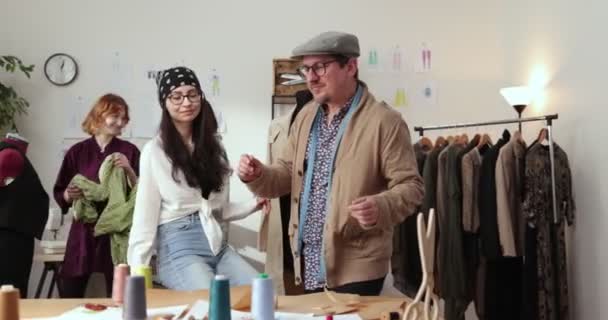 งานของนักออกแบบแฟชั่นและผู้ดูแลในร้าน นักออกแบบแฟชั่นทํางานในสตูดิโอของพวกเขา ผ้าที่มีสีสัน, เสื้อผ้าแขวนและเย็บรายการที่มองเห็นได้ . — วีดีโอสต็อก